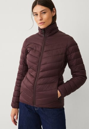 Bordeaux pufferjakke med høj krave, horisontal syningsdesign, lynlåslukning og sidelommer, parret med mørke denimbukser.
