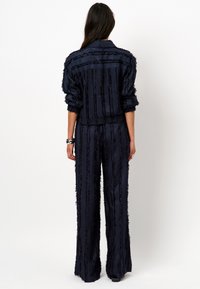 Navyblauwe tweedelige set met een franjestructuur en verticale strepen. De blazer heeft een kraag en losse mouwen, gecombineerd met wijde broekspijpen.