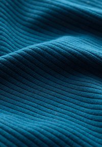 Getextureerde ribbelstof in tealblauw, met subtiele variaties in diepte. Gladde oppervlakte met een zachte uitstraling, ideaal voor kleding of bekleding.