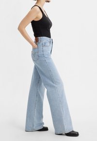 Ljust blå vida jeans gjorda av denim med hög midja. Har bakfickor och en brun läderlapp på midjebandet.