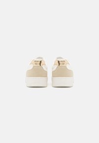 Beige suede and white synthetic sneakers with a glossy gold accent. Rounded toe, low profile design with textured heel and padded collar.