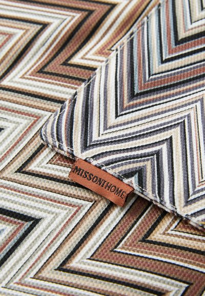 To teksturerte stoffbiter med flerfargede sikksakk-mønstre i brunt, beige, svart og hvitt, som har en brun "MISSONIHOME"-etikett.