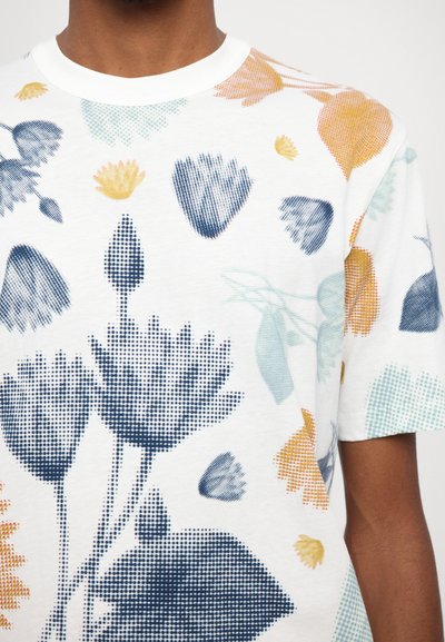 White cotton t-shirt featuring a multicolored floral pattern with blue, yellow, and green accents, short sleeves, and a crew neckline.