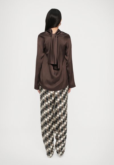 Top din satin maro cu mâneci lungi și detaliu cu fundiță la spate, asortat cu pantaloni largi cu un model de tablă de șah bej și maro.