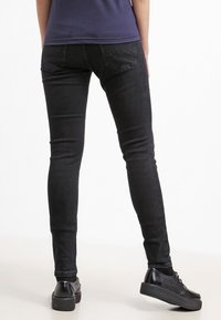 Chude czarne dżinsy o gładkiej teksturze, pięć kieszeni, kontrastowe przeszycia na tylnych kieszeniach. Noszone z czarnymi butami na platformie.