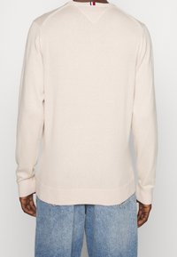 Lichtbeige trui met lange mouwen, een gladde textuur, geribbelde zoom en manchetten, met een kleine rode, witte en blauwe accent aan de nek.