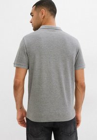 Maglietta polo grigia realizzata in un tessuto morbido, con colletto classico e maniche corte, caratterizzata da una texture liscia e priva di motivi visibili.