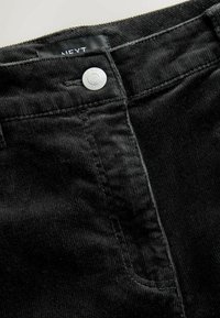 Pantaloni din catifea neagră cu închidere cu buton argintiu, țesătură texturată, dungă verticală și o etichetă cu inscripția "NEXT" aproape de talie.