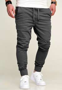 Gray joggers made of soft fabric, featuring an elastic waistband with drawstrings and ribbed cuffs, paired with white sneakers.