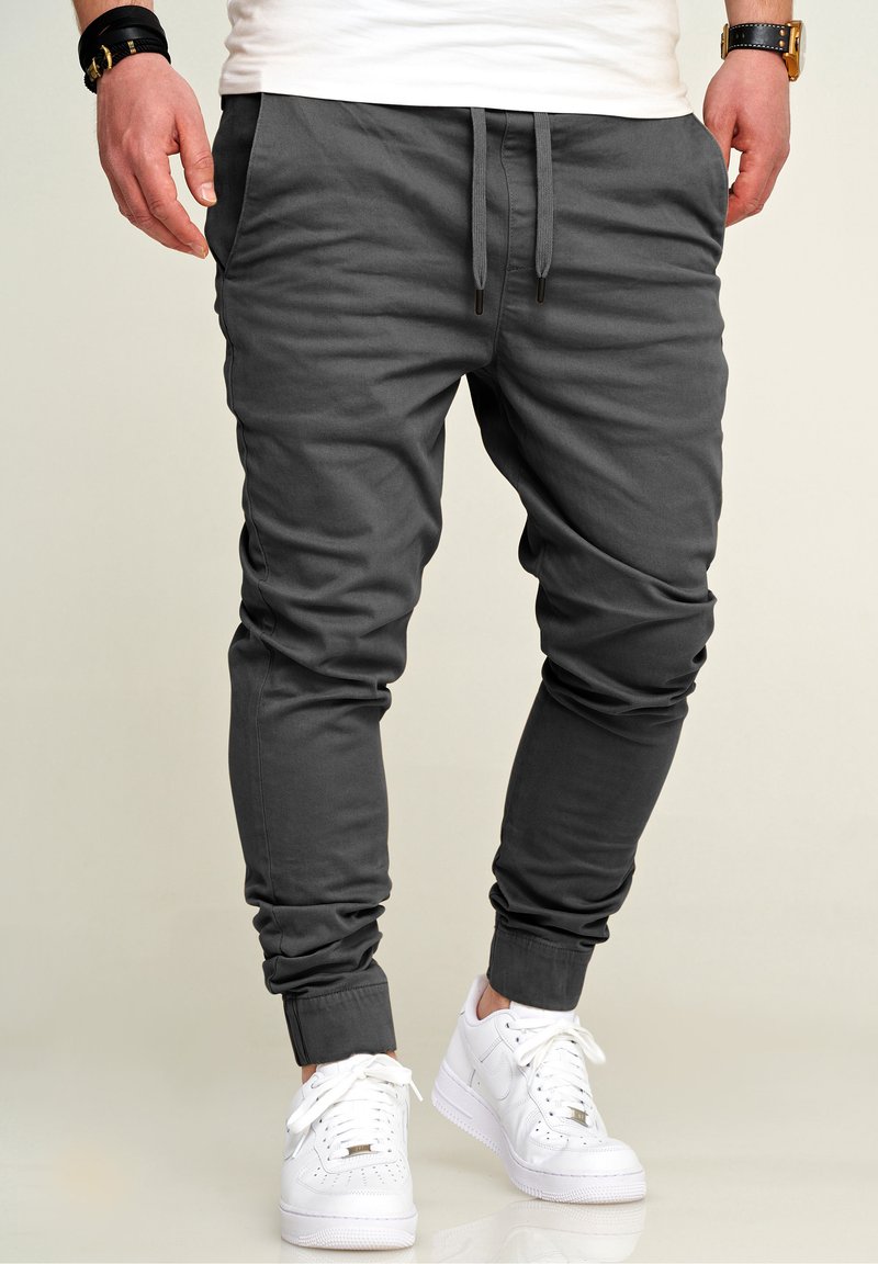 Gray joggers made of soft fabric, featuring an elastic waistband with drawstrings and ribbed cuffs, paired with white sneakers.