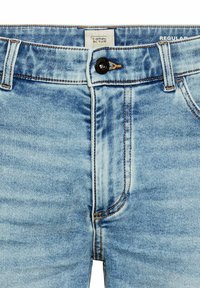 Jean en denim bleu clair avec une coupe standard, dotés d'une fermeture à bouton, de coutures contrastantes et d'un design de poche classique.