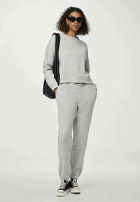 Siva bombažna sweatshirt in usklajeni jogger hlače z elastičnimi manšeti, okroglo ovratnikom in sproščenim fitom. V kombinaciji z črnimi sončnimi očali in supergami.