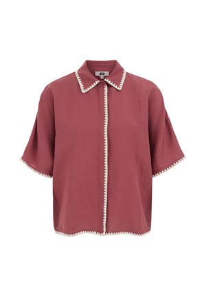 Camicia rosa polvere a maniche corte con bordatura a zigzag bianca su collo, patta frontale, maniche e orlo, con un solo bottone superiore visibile.