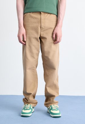 Beige cotton pants with a relaxed fit, featuring side pockets and a smooth texture, paired with green and cream sneakers.