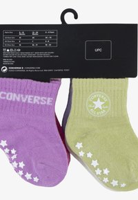 Lila és zöld zoknik bordás textúrával, fehér csillagmotívumokkal, és a zöld zoknin a "CONVERSE ALL STAR" felirattal.