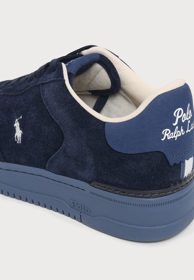 Σκούρο μπλε σουέντ αθλητικό παπούτσι Polo Ralph Lauren με λευκό κεντημένο λογότυπο, κρεμανό μαξιλαράκι στον γιακά και αντίστοιχη μπλε σόλα με ανάγλυφο "Polo".