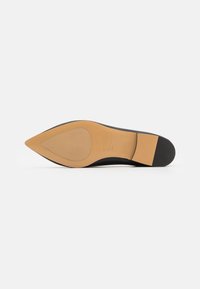 Zapato negro de punta afilada con un exterior liso, suela marrón y un ligero tacón; presenta un acento de goma duradera en el tacón para mayor tracción.