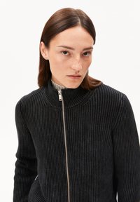 Schwarzer, gerippter Reißverschluss-Pullover mit hohem Kragen und strukturiertem Stoff. Silberner Reißverschluss an der Vorderseite sorgt für Details.