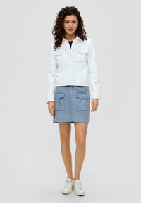 Witte denimjas met twee voorzakken, gecombineerd met een blauwe rok met twee grote opgestikte zakken. Gedragen met witte sneakers.