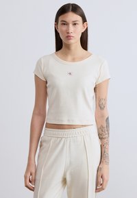 Κοντοκομμένο ριμπ μπλουζάκι σε εκρού απόχρωση με στρογγυλή λαιμόκοψη και κοντά μανίκια. Διαθέτει μικρό κεντημένο λογότυπο στο στήθος.