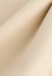 Beiger Stoff mit einer glatten Textur, der subtile Rippungen und einen sanften Glanz aufweist, in sanften Falten angeordnet.