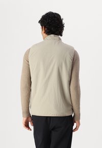 Beige vest with a smooth, lightweight exterior and textured, knit sleeves in a soft tan color. Features a high collar and ribbed cuffs.