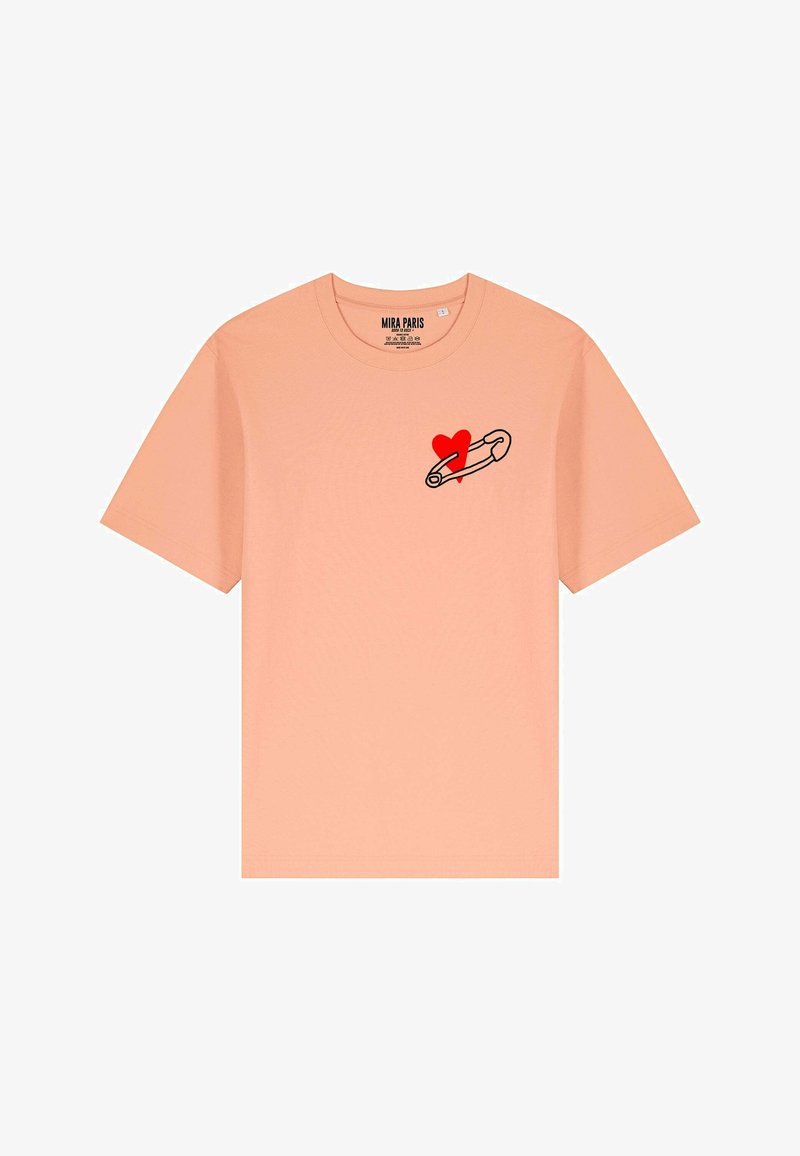 Peachkleurig t-shirt met korte mouwen, voorzien van een zwarte omlijning speld en een rode hartafbeelding op de linkerborst.