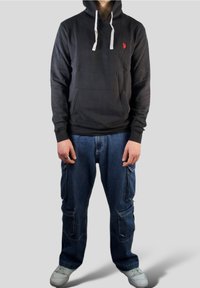 Czarna bluza z kapturem z przednią kieszenią i białymi sznurkami; w zestawie luźne niebieskie dżinsowe spodnie cargo. Obuwie to białe trampki.