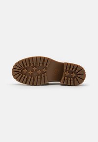 Semelle de botte en caoutchouc marron avec des motifs de bande de roulement profonds, rectangulaires et en forme de croix, vue de dessous sur un fond blanc.
