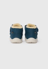 Bottines en suède bleu avec une doublure en fourrure crème, une sangle ajustable et des semelles en caoutchouc blanches. Texture lisse avec un matériel minimal.