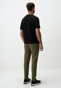 Czarna koszulka z krótkim rękawem, oliwkowe dresy, strukturalny materiał, dopasowany krój, noszona z czarnymi butami sportowymi, widok z tyłu.