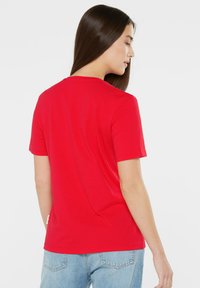 Red short-sleeve t-shirt featuring a round neckline, smooth texture, and a tag on the side. The back view shows a simple, classic design.