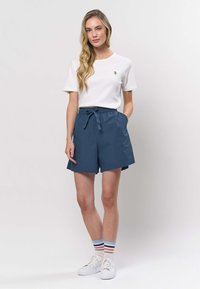 Valkoinen, ribbattu lyhythihainen t-paita, jossa pieni kirjailu, yhdistetty sinisiin korkeavyötäröisiin shortseihin ja valkoisiin tennareihin, joissa moniväriset raitasukat.