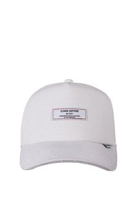 Weißer Hut aus strukturiertem Stoff. Hat einen gebogenen Schirm und ein rechteckiges Etikett mit roten Nähten, das Markendetails enthält.