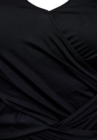 Haut noir enroulé en tissu lisse, doté d'un décolleté en V profond et de détails de couture complexes le long des coutures. Le matériau est légèrement texturé.