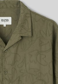 Chemise vert olive avec un motif d broderie florale texturée, dotée d'un col et d'une fermeture à boutons. L'étiquette indique "Bzb, M."