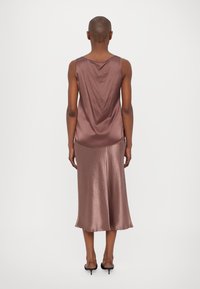 Satin slip dress in dusty rose, featuring a draped back, sleeveless design, and a flowy silhouette that ends just below the knee.