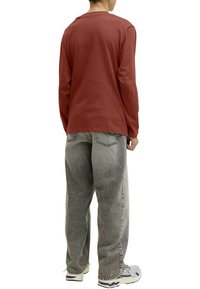 Chemise à manches longues de couleur rouille avec une coupe décontractée, associée à un jean gris délavé. Le jean présente une légère texture usée.