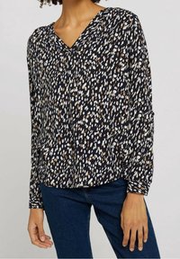 Blouse ample en marine, avec un motif à pois blancs et beige. Encolure en V et manches longues avec poignets boutonnés. Tissu doux.