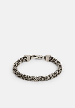 Náramek ze stříbrného kovu s propojenými články a zapínáním na karabinu na světlém pozadí.