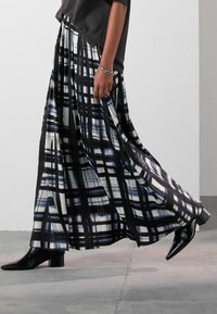 Gonna lunga in bianco e nero con motivo a griglia, realizzata in un tessuto fluido. Abbinata a stivali neri alla caviglia. Texture liscia e vestibilità rilassata.