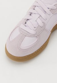 Lys lilla sneaker med en blanding av semsket skinn og syntetisk lær, teksturert gummisåle, rund tå og flate lisser med preget detaljer.