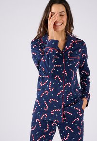 Conjunto de pijama navy con un patrón de bastones de caramelo y pequeños corazones. Fabricado con tela suave, con ribete rojo y detalles de botones en la camisa.