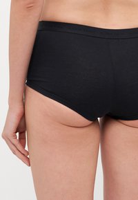 Black cotton hipster underwear with a smooth texture and a wide elastic waistband featuring embossed branding. Side view showcases fit and cut.