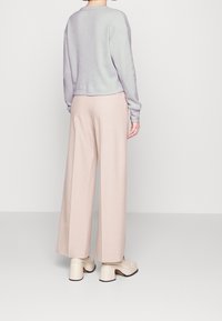 Korte lavendelkleurige trui met ribbeltextuur, gecombineerd met lichtroze wijde broek. Chunky beige hakken maken de outfit af.