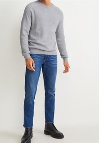 Szary sweter z dzianiny z okrągłym dekoltem, zestawiony z niebieskimi dżinsami i czarnymi botkami na sznurowadła. Charakterystyczne prążkowane mankiety i linia talii.