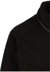 Primo piano di una giacca in pile nera, con una superficie testurizzata e a anelli e un design con collo alto, completo di un bordo a contrasto lungo il colletto.