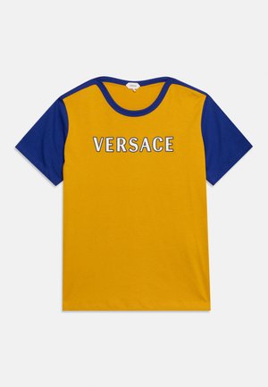 T-shirt jaune avec manches et col bleus, avec "VERSACE" en lettres majuscules blanches sur la poitrine.
