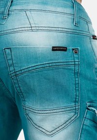 Jean en denim bleu clair avec un design délavé, des poches arrière avec des coutures noires et une étiquette logo CIPO & BAXX.