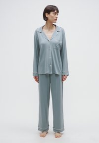 Világoskék pizsamaszett puha anyagból; hosszú ujjú, gombos felső zsebbel és nadrágszárak kontrasztos szegéllyel, bő szabásban.